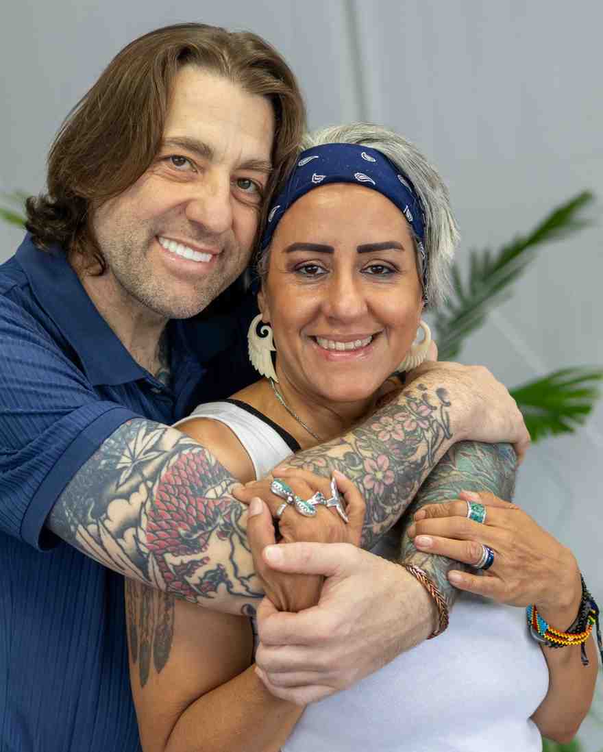 A smiling man and woman, both with visible tattoos, embrace closely for a joyful close-up portrait.