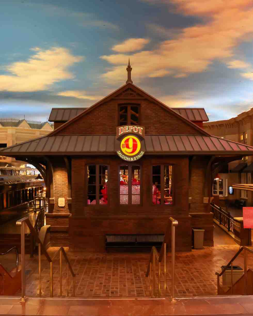Exterior of the Depot #9 Saloon & Stage, a brick building with a lit sign, photographed at dusk under a colorful sky.